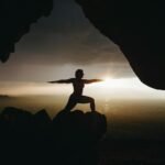 silhouette of person in yoga post on top of cliff during sunset