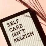 Letter board displaying 'Self Care Isn't Selfish' with artistic shadow on pink background.