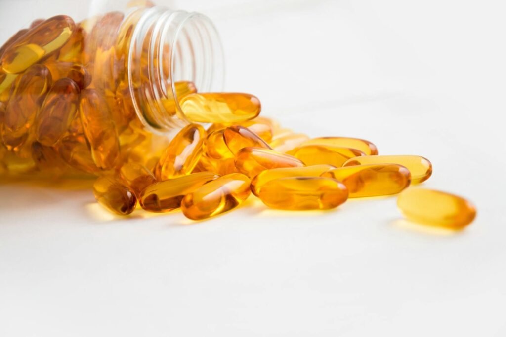 Close-up of fish oil capsules spilling from a bottle on white background.