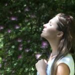 A woman enjoying a serene moment in a sunlit garden, surrounded by vibrant flowers.