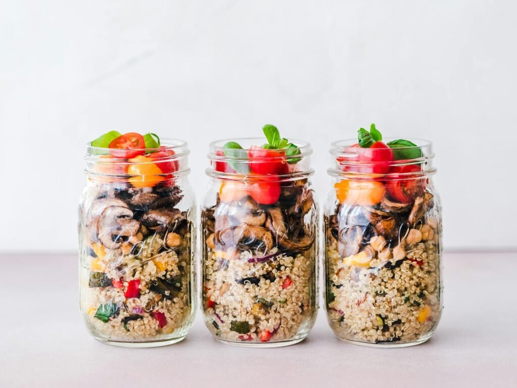 Three jars of colorful quinoa salad with mushrooms and tomatoes, perfect for a healthy meal.